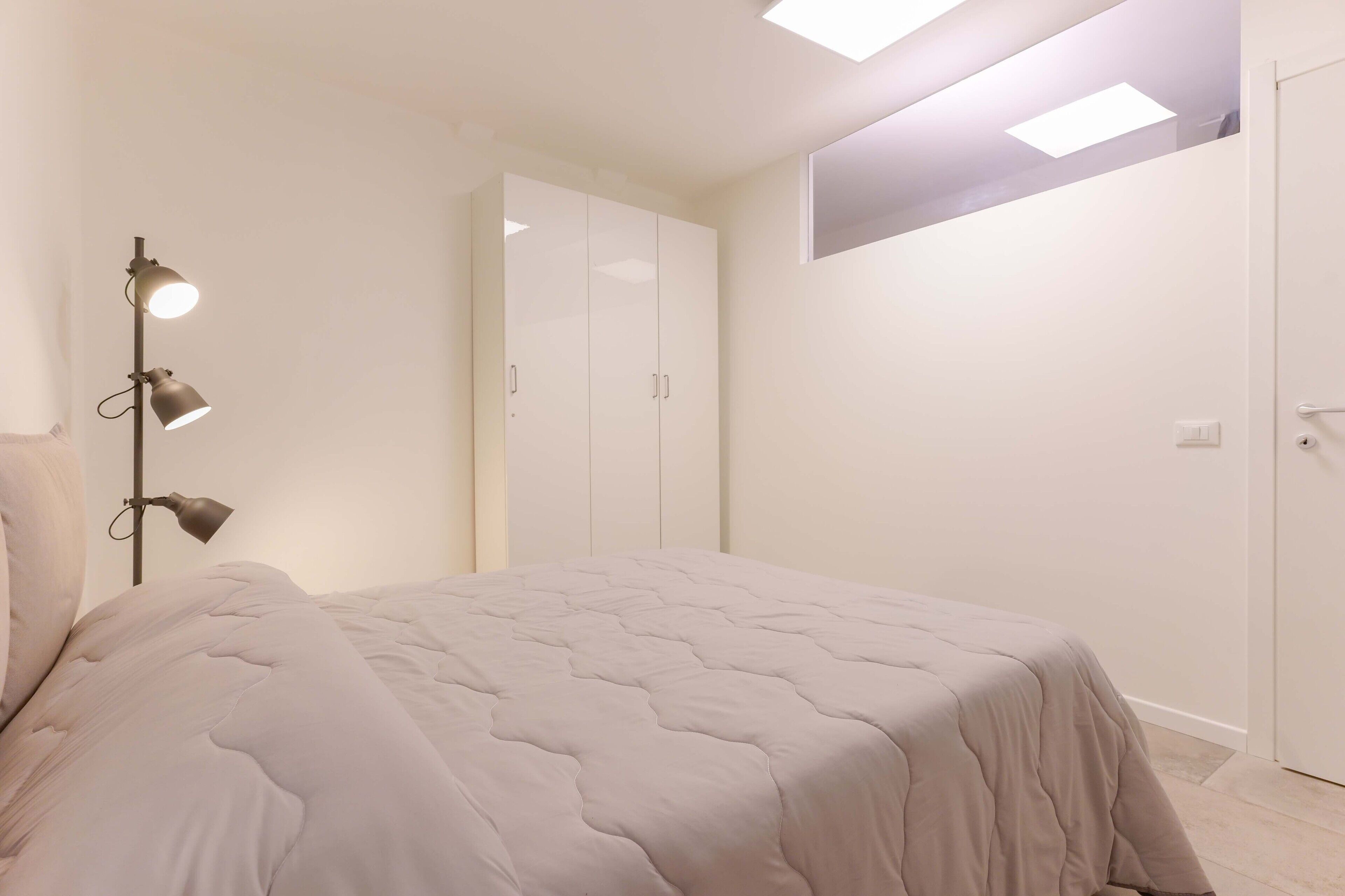 A bedroom with a bed, a nightstand, a lamp, and a wardrobe.