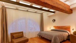 Un dormitorio con cama, sofá, techo de madera y un ventanal con cortinas.