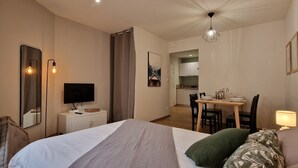A hotel room with a bed, a desk, a chair, a television, and a dining area with a table and chairs. - Le T2 A du Meysse (Meysse)