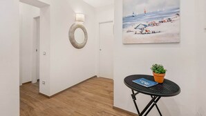 Een gang met een ronde spiegel, een schilderij van een strandgezicht en een kleine tafel met een plant en een tijdschrift.