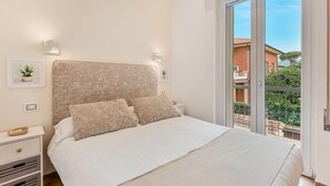 Een slaapkamer met een groot bed, twee nachtkastjes, een raam met uitzicht op gebouwen en een balkon.