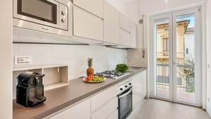 Een moderne keuken met een gasfornuis, magnetron en oven, een koffiezetapparaat, en uitzicht op een gebouw door een glazen deur.