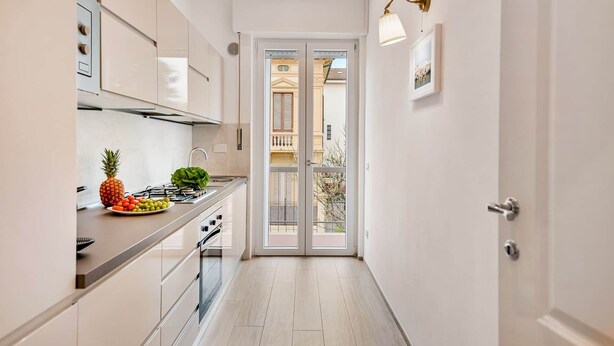 Een smalle keuken met uitzicht op een balkon, een fornuis en een spoelbak.
