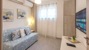 Een woonkamer met een gestreept bankje, een aan de muur bevestigde televisie en een plafondlamp.