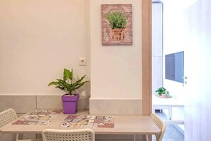 A dining area with a table, chairs, a purple plant, and a wall-mounted artwork. - Your perfect choice in Athen's best location 1 (Athina)