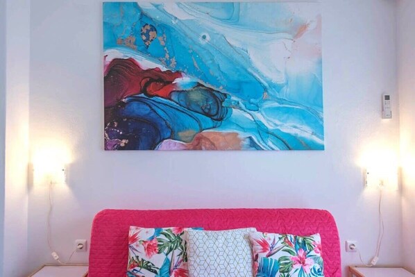 A bedroom with a bed, a colorful abstract painting on the wall, and a nightstand with a lamp. - Your perfect choice in Athen's best location 1 (Athina)