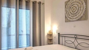 Ein Hotelzimmer mit Bett, Vorhängen, einem Wandbild und einem Nachttisch mit Lampe.