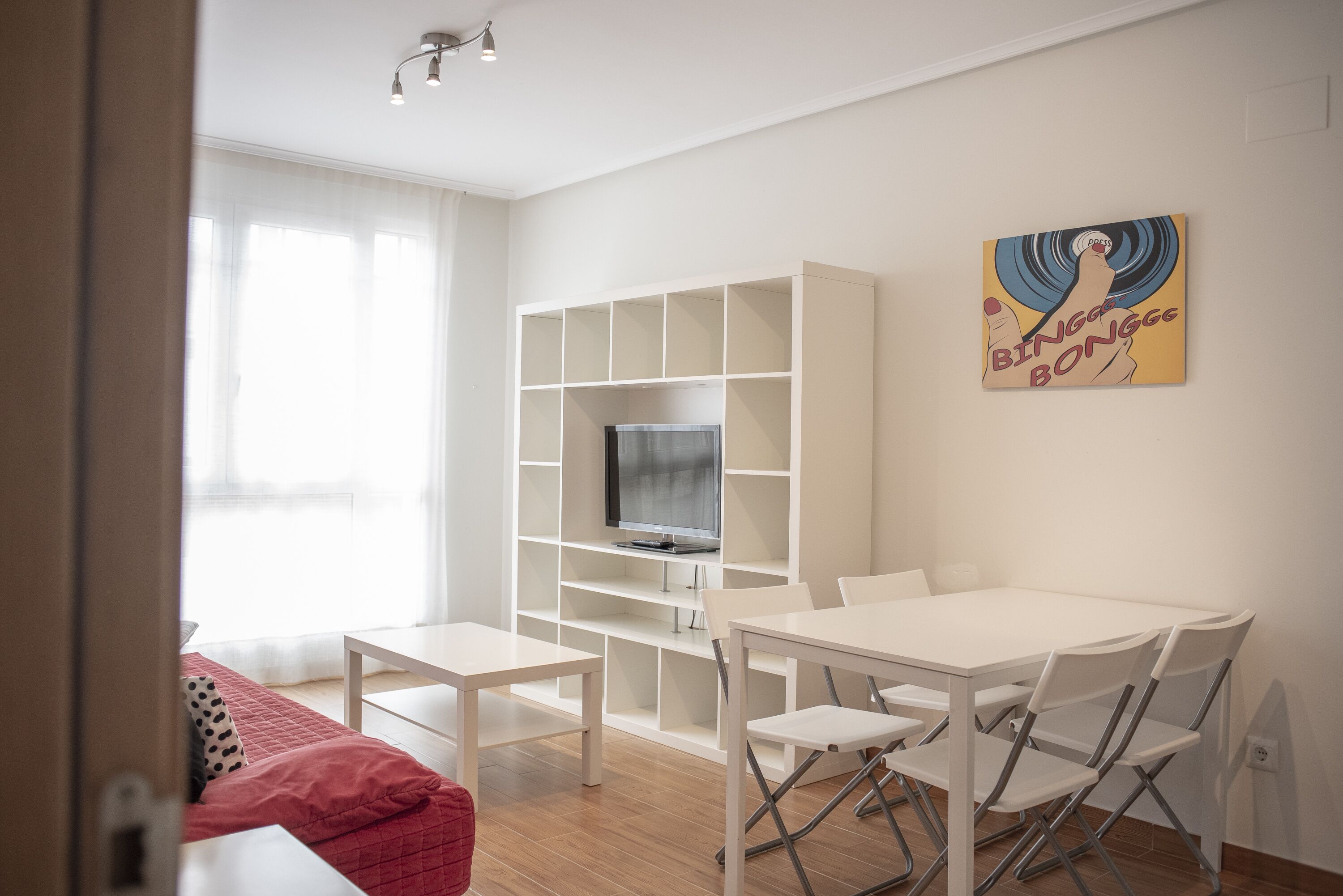 Een moderne woonkamer met een witte tv-meubel, een eettafel met stoelen en een rode bank.