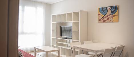 A modern living room with a white TV stand, a dining table with chairs, and a red sofa.