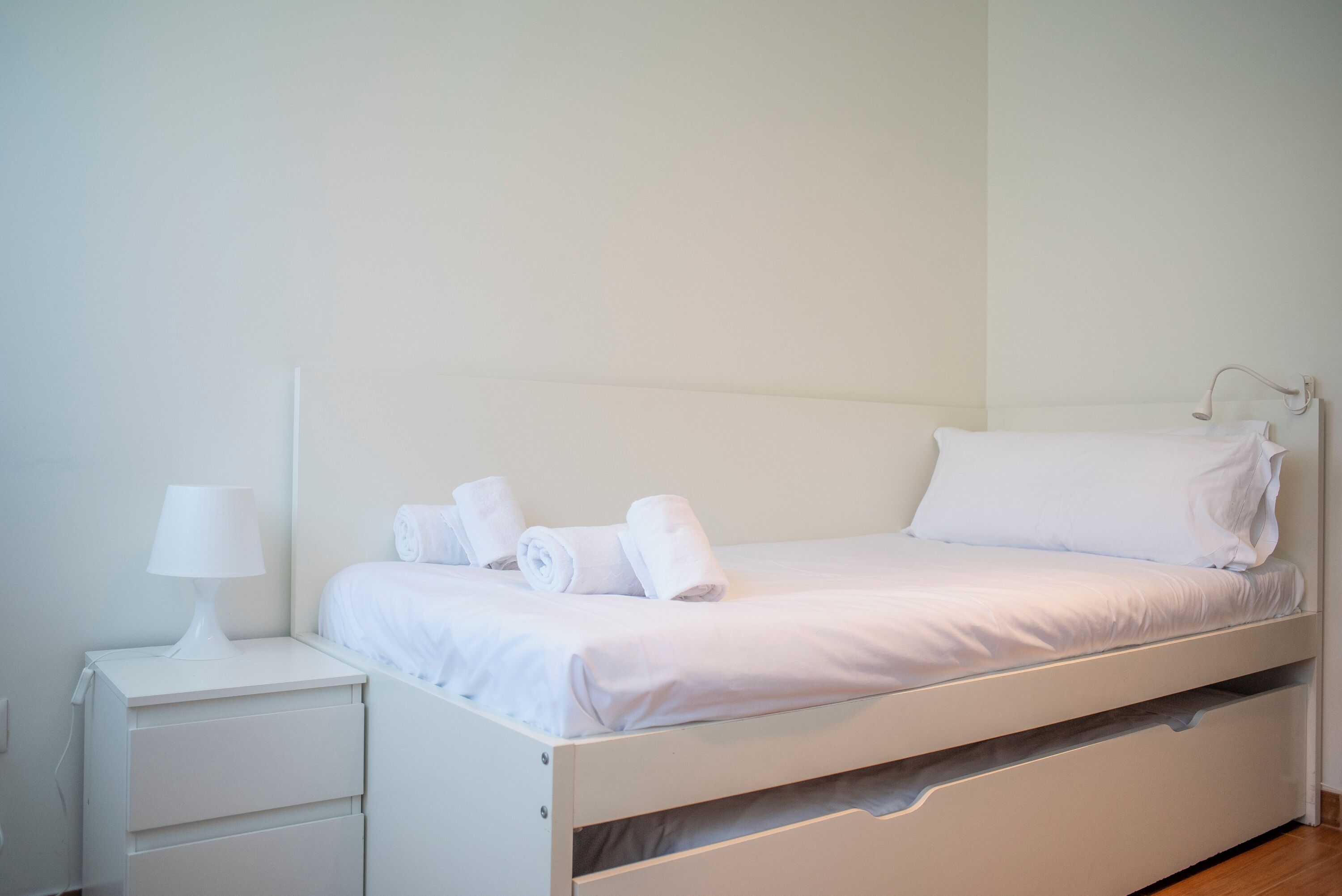 Habitación con cama individual, una mesita de noche con lámpara y toallas dobladas cuidadosamente.