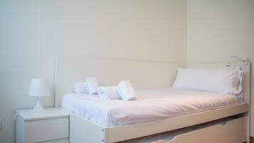 Habitación con cama individual, una mesita de noche con lámpara y toallas dobladas cuidadosamente.