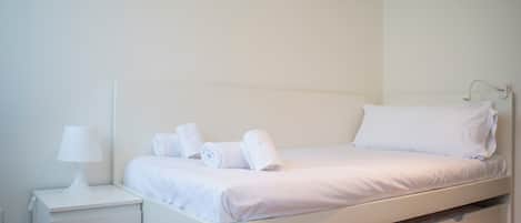 Habitación con cama individual, una mesita de noche con lámpara y toallas dobladas cuidadosamente.