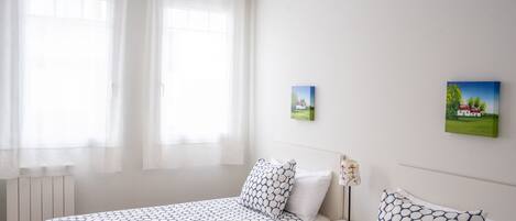 A hotel room with two beds, a nightstand, a lamp, and two small paintings on the wall.
