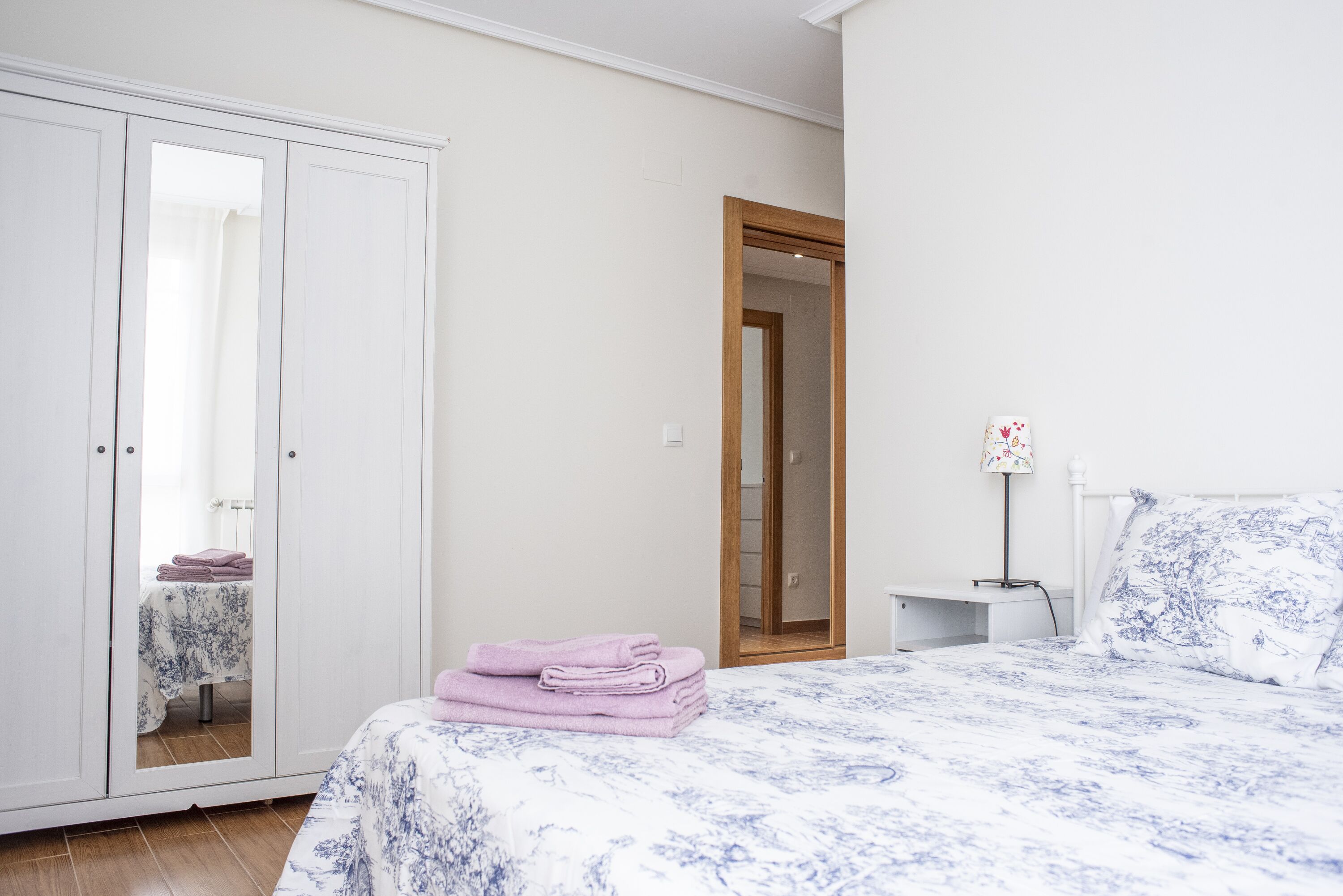 A bedroom with a bed, a wardrobe, a nightstand, and a mirror.