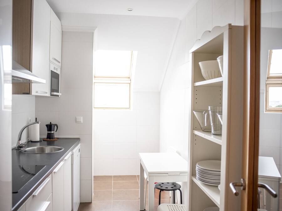 A compact kitchen with white cabinets, a stainless steel sink, and a small dining table.