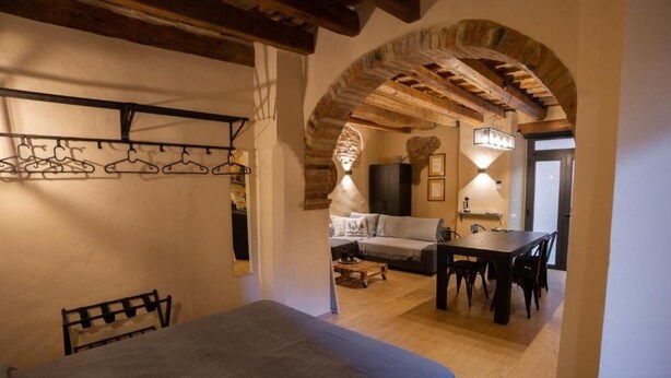 A cozy room with a bed, a dining table, and a sofa. There is a wooden ceiling and an arched doorway leading to another room.