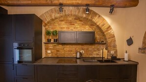 A kitchen with dark cabinetry, a built-in oven, a brick arch, and pendant lighting.