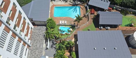 Ett flygbildsfoto av ett bostadsområde med en swimmingpool, en liten trädgård och en byggnad med ett sluttande tak.