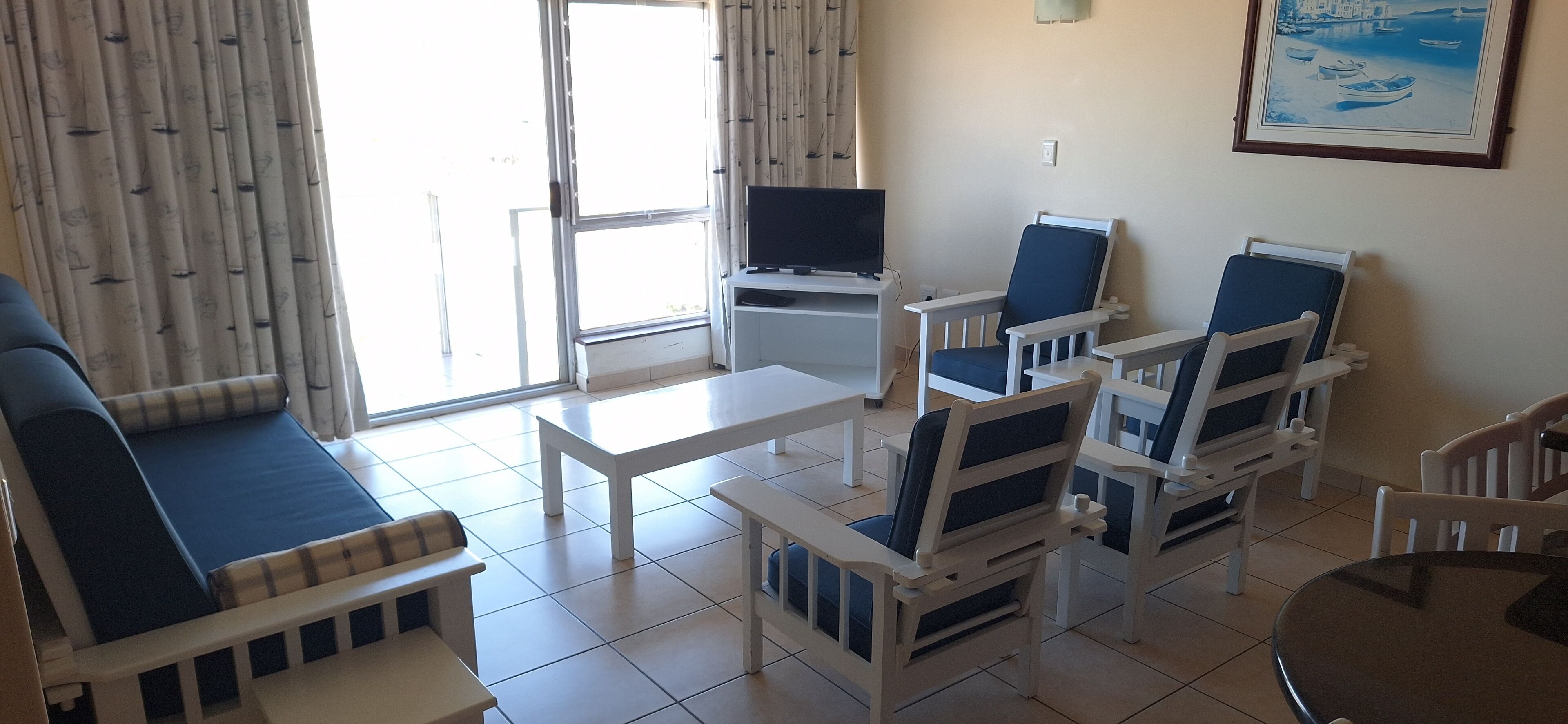 Una sala de estar con sofá, sillas, una mesa de centro y un televisor sobre un mueble.
