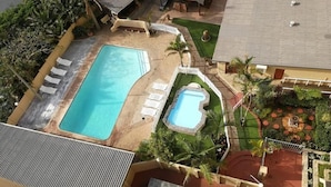 Un área de piscina en la azotea con dos piscinas, sillas de descanso y un pequeño jardín.