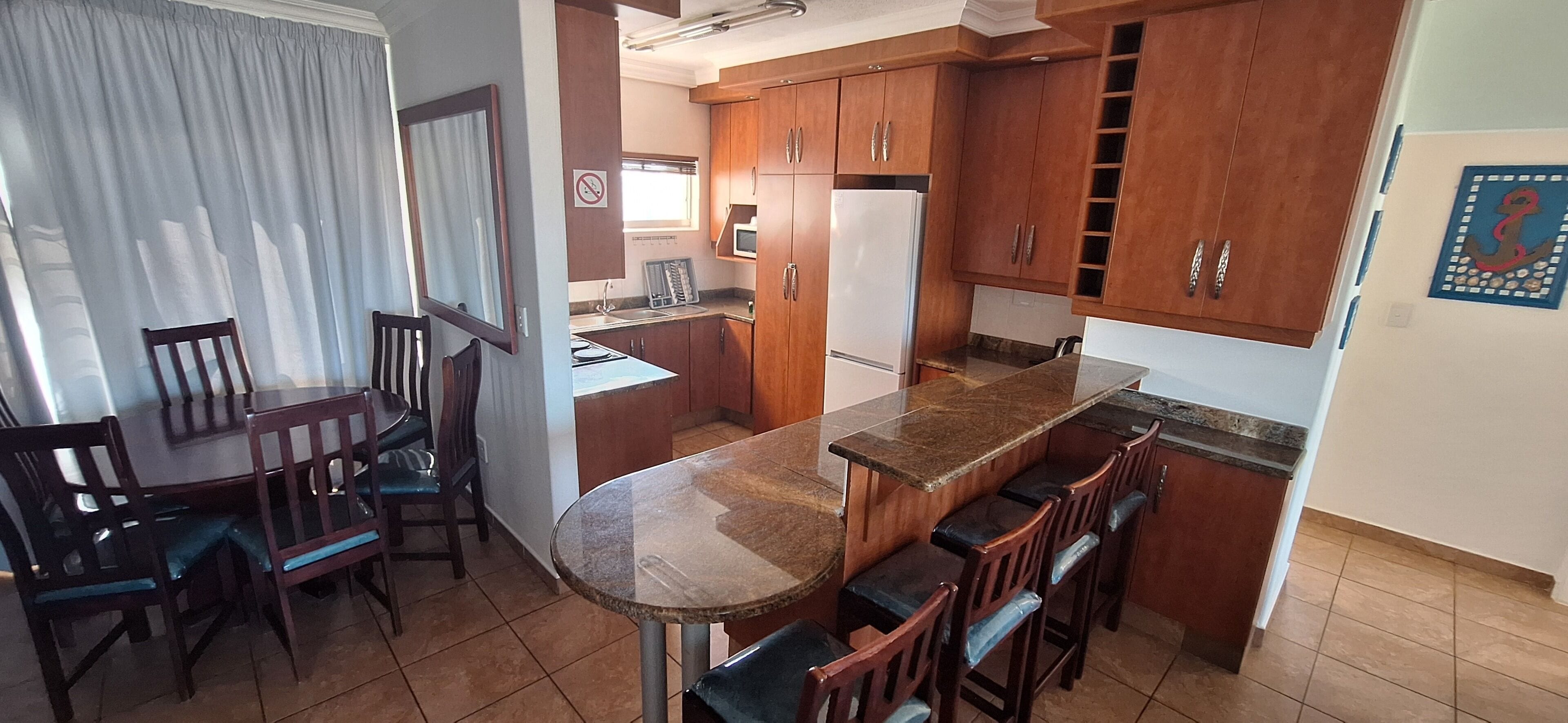 A compact kitchen with wooden cabinets, a granite countertop, and a dining area with chairs.