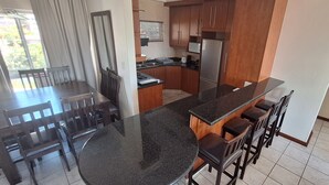 Una cocina moderna con encimera de granito, armarios de madera, refrigerador de acero inoxidable y un comedor con mesa y sillas.