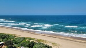 Una playa con olas, cielo despejado y un barco a lo lejos.