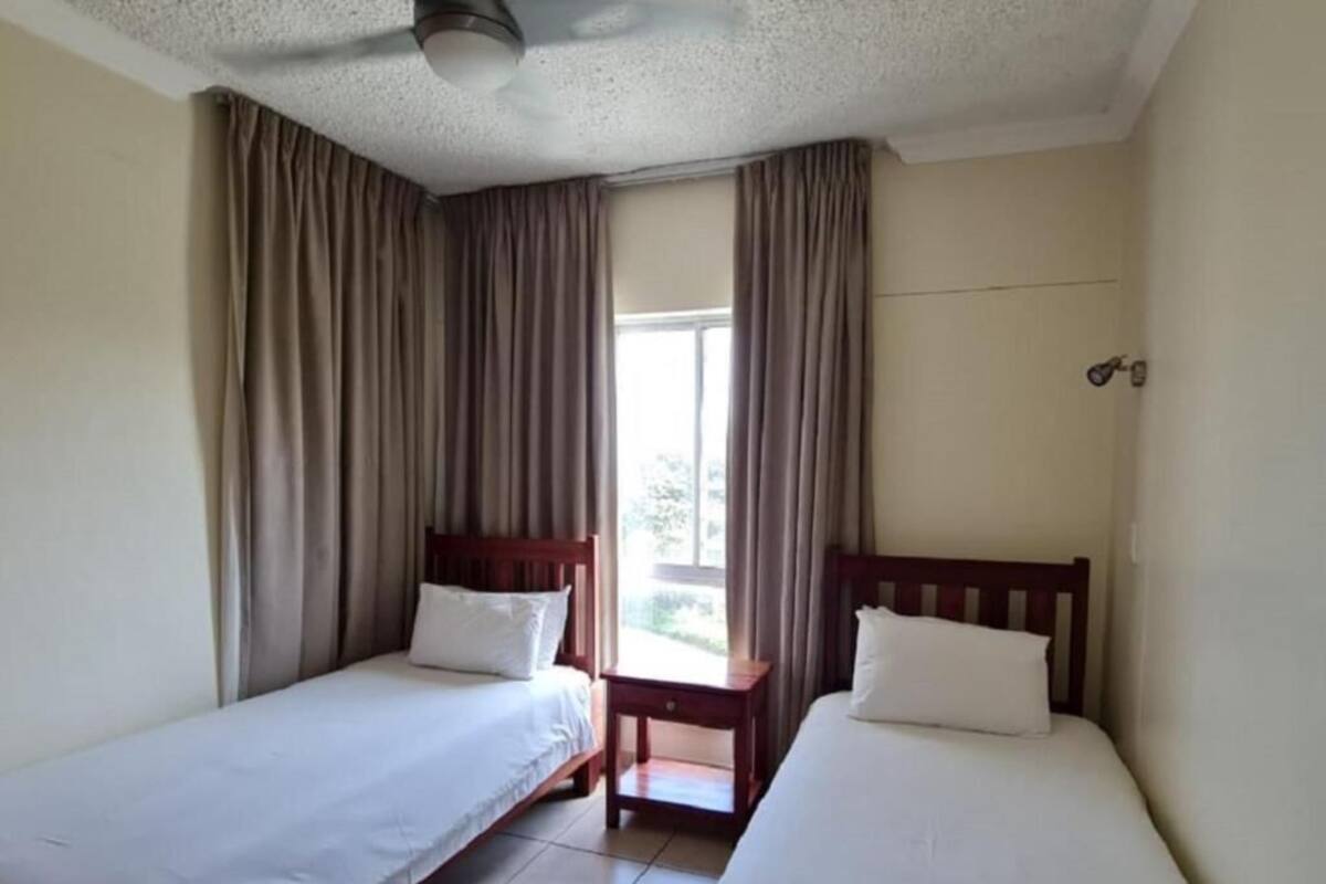 A room with two single beds, a small table, and a window with curtains.