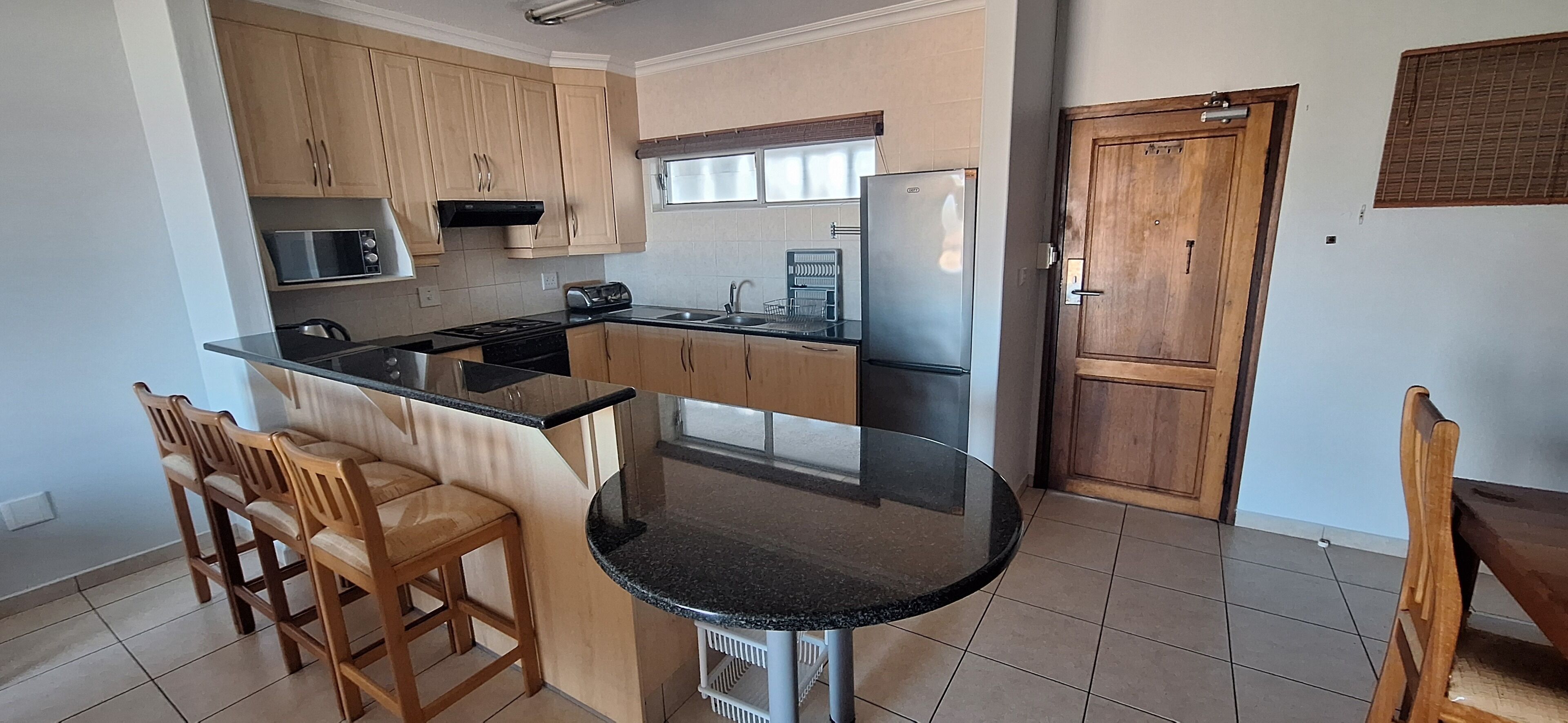 A kitchen with wooden cabinets, a black countertop, a stainless steel refrigerator, and a window.