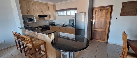 A kitchen with wooden cabinets, a black countertop, a stainless steel refrigerator, and a window.