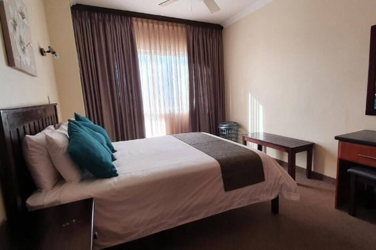 A hotel room with a bed, a desk, a chair, a mirror, and a window with curtains.