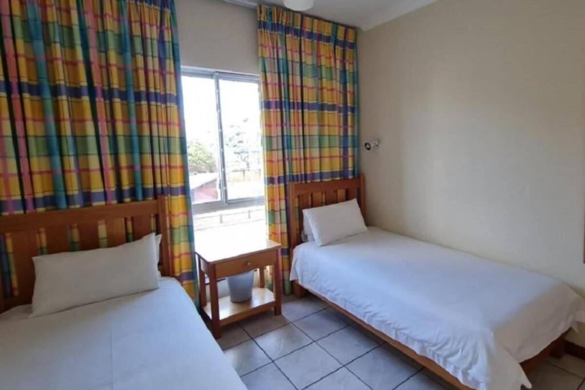 A room with two single beds, a wooden headboard, a small table, and colorful curtains.