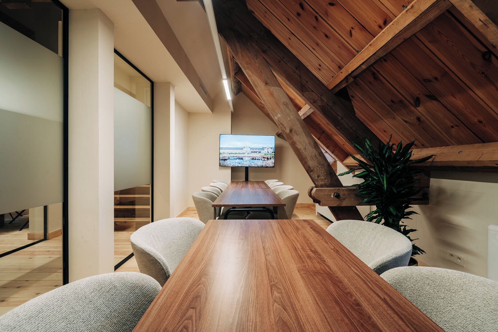 Une salle de conférence avec une table en bois, des chaises, un téléviseur et un escalier.