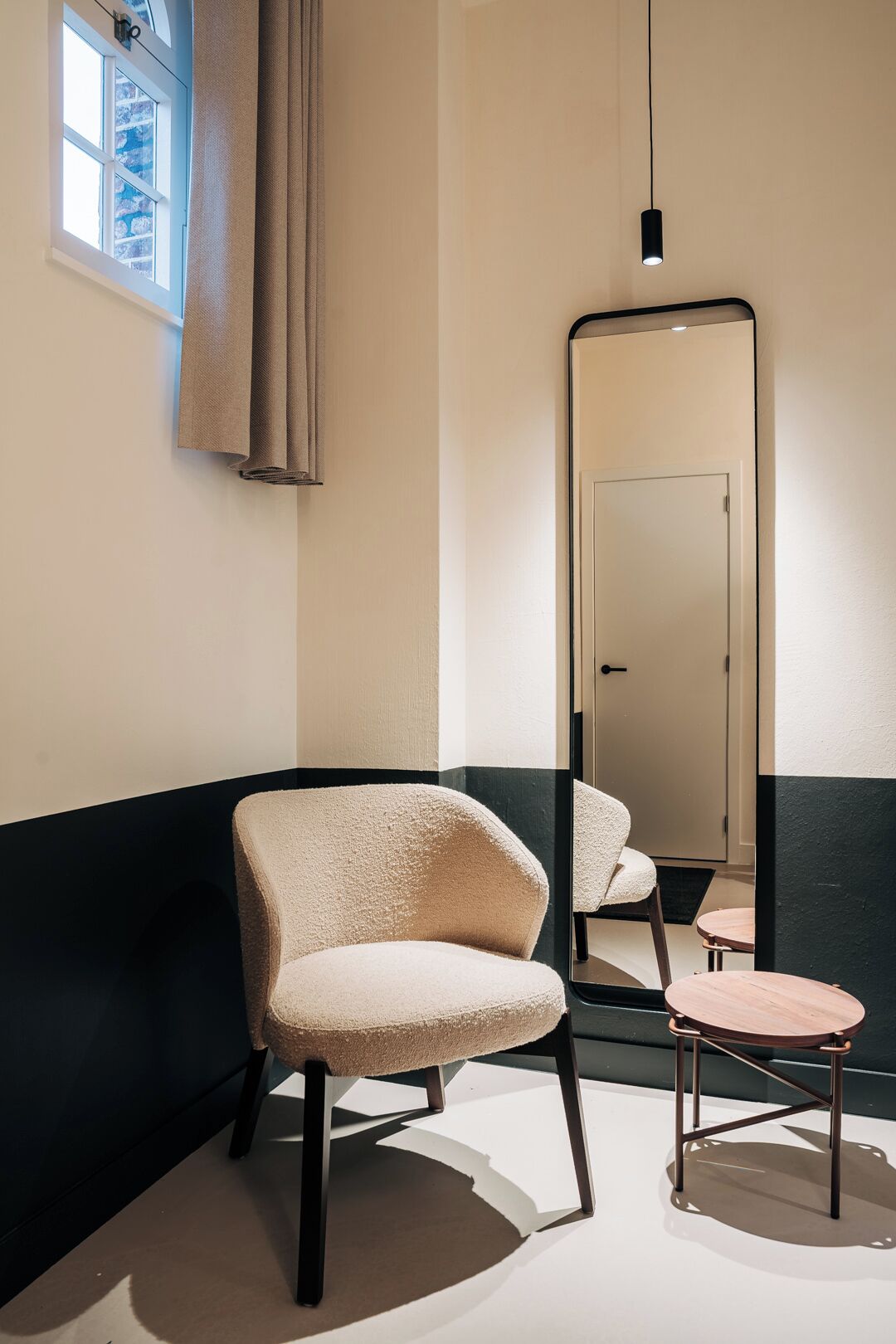 A room with a large mirror, a chair, a small table, and a window with curtains.