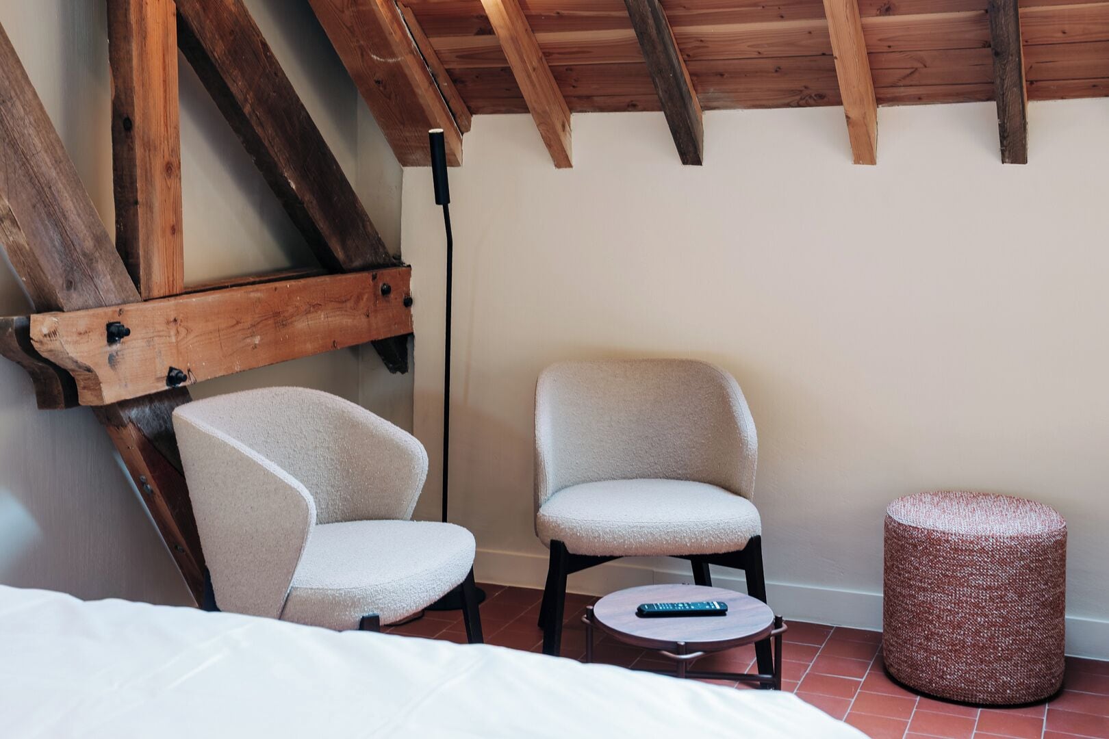 A room with a bed, two chairs, a small table, and a round ottoman.