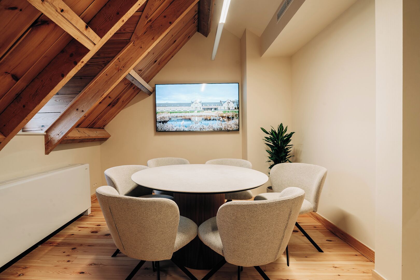 Un salón de conferencias con una mesa redonda y seis sillas, un ventanal con vista a un edificio y un techo de madera.