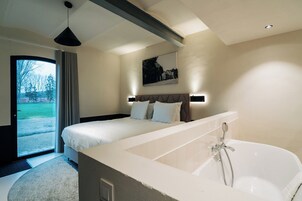 Una habitación de hotel moderna con una cama grande, una bañera y vistas al exterior.