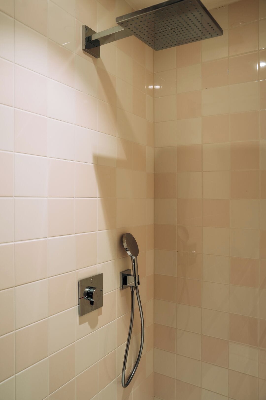 A shower with a handheld showerhead and a wall-mounted control panel.