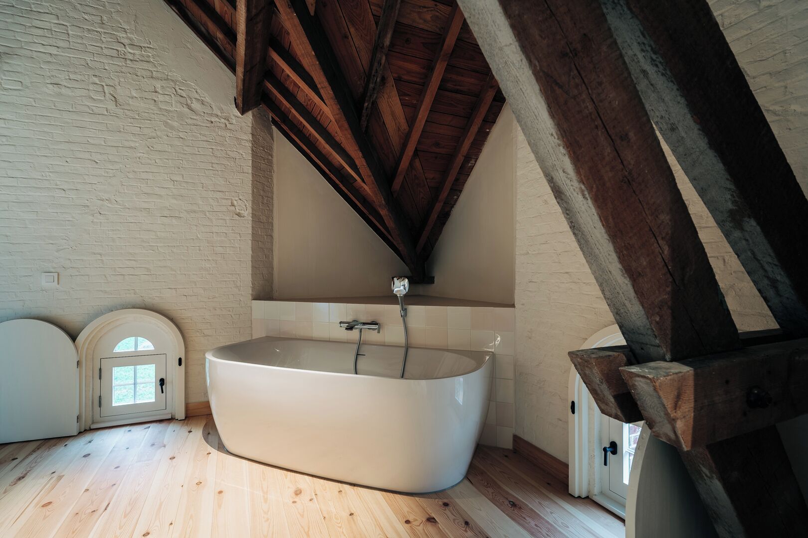 A room with a large bathtub, wooden beams, and a white brick wall.