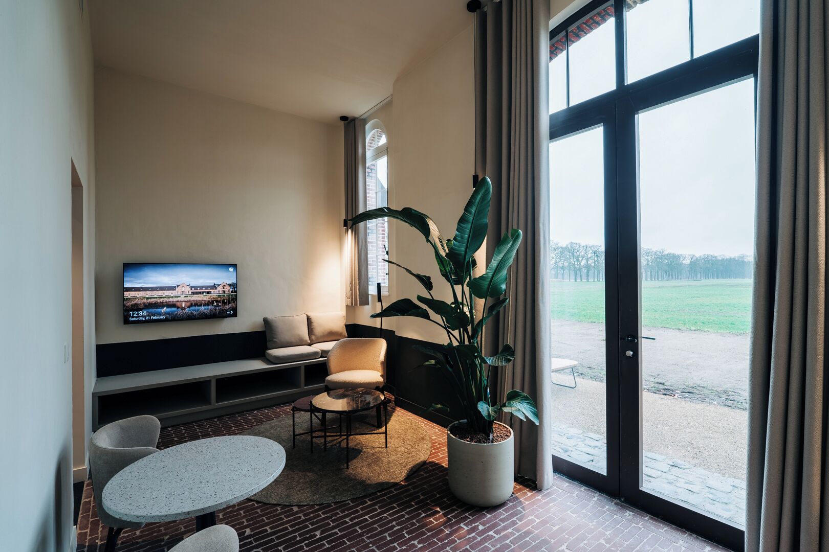 Ein modernes Wohnzimmer mit Fernseher, Sitzgelegenheiten, einem Blumentopf und Blick durch große Fenster.