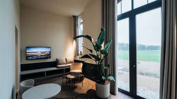 Ein modernes Wohnzimmer mit Fernseher, Sitzgelegenheiten, einem Blumentopf und Blick durch große Fenster.