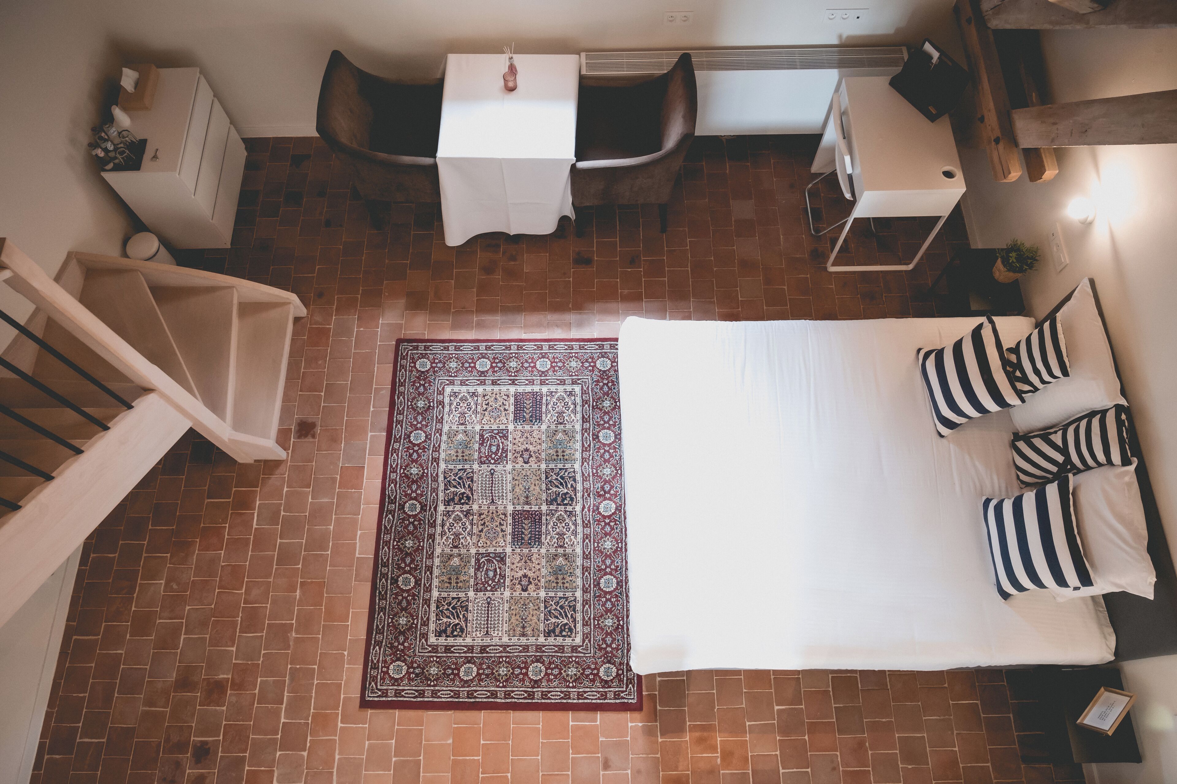 A bedroom with a large bed, a patterned rug, a chair, and a small table.
