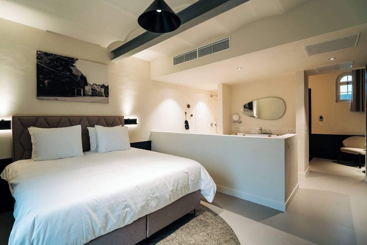 A modern bedroom with a large bed, a bathroom with a vanity, and a ceiling with exposed beams.
