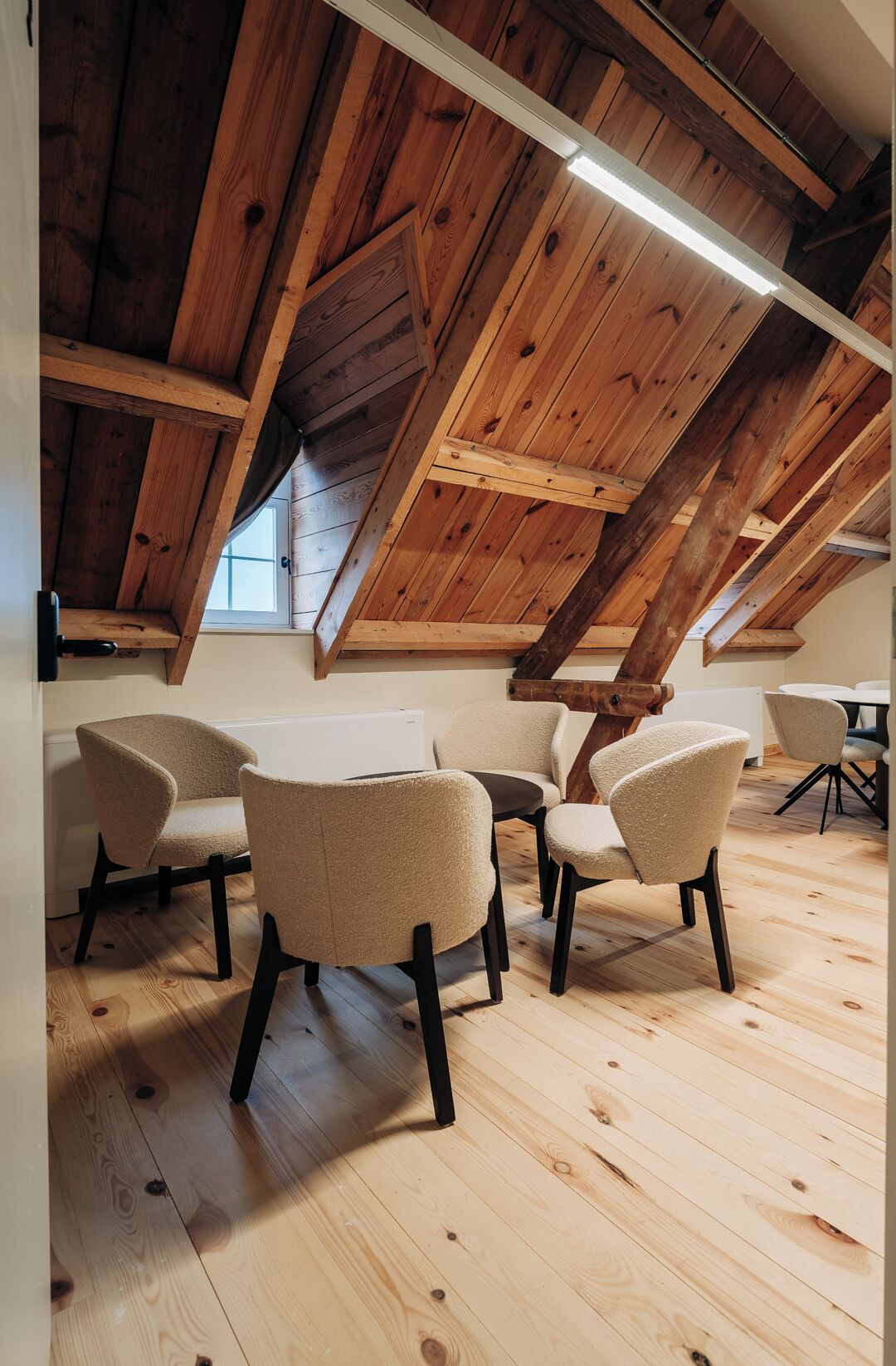 Una habitación con vigas de madera, techo inclinado y una mesa con sillas.