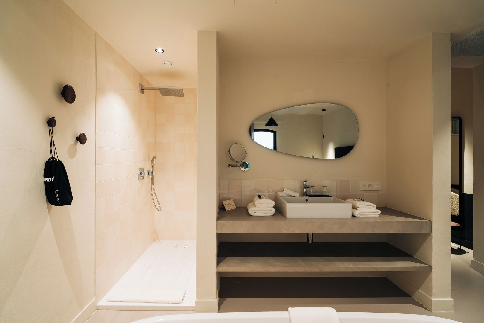 Ein modernes Badezimmer mit bodenebener Dusche, großem Spiegel und Waschtisch mit Spüle und Handtuchhalter.