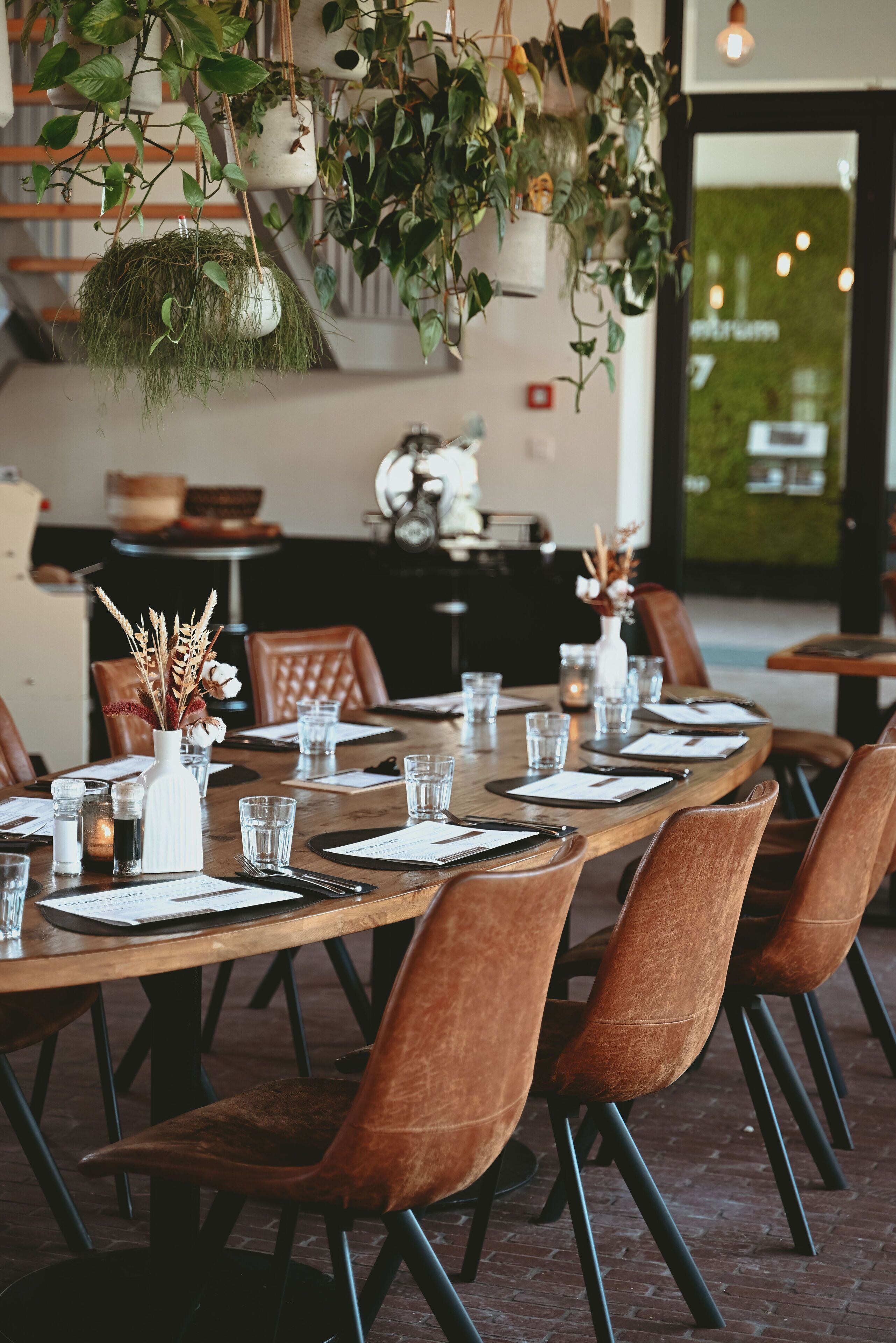 A dining area with a long wooden table set for six, surrounded by brown upholstered chairs.