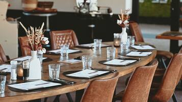A dining area with a long wooden table set for six, surrounded by brown upholstered chairs.