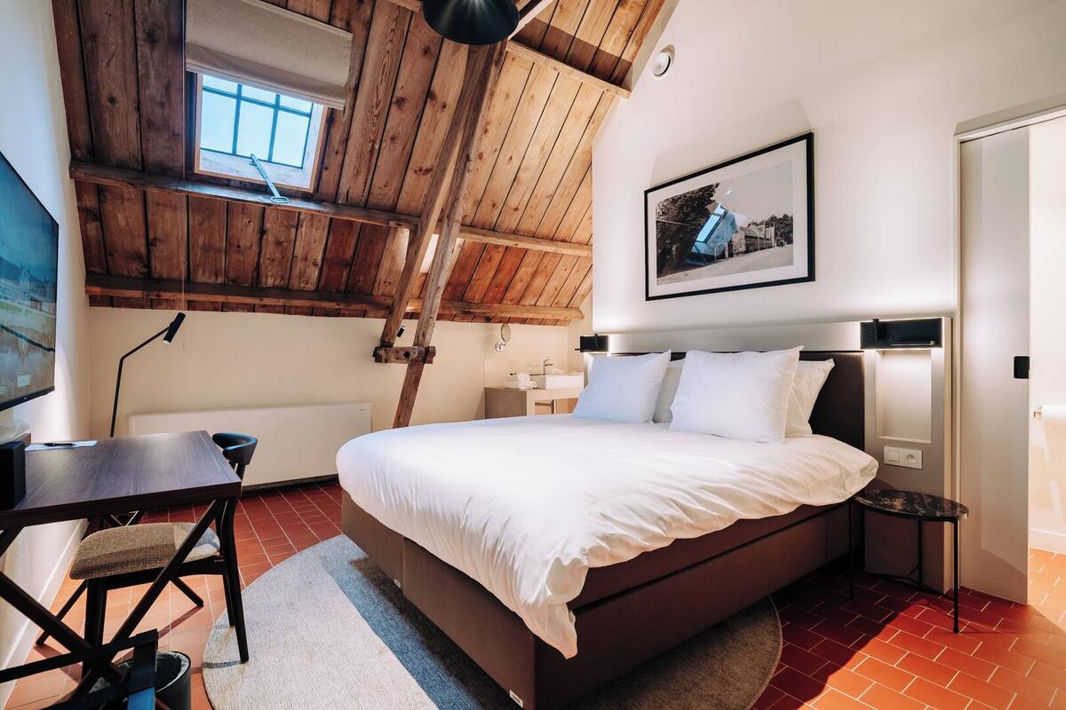 A bedroom with a wooden ceiling, a bed, a desk, and a chair.