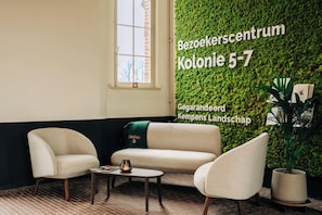 A modern interior with a green wall, a sofa, two armchairs, a small table, and a potted plant.