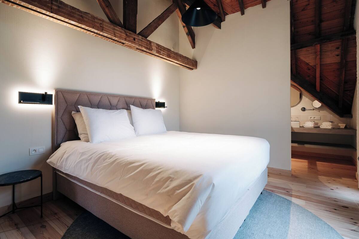 A bedroom with a bed, bedside tables, a headboard, and a view of a wooden staircase.